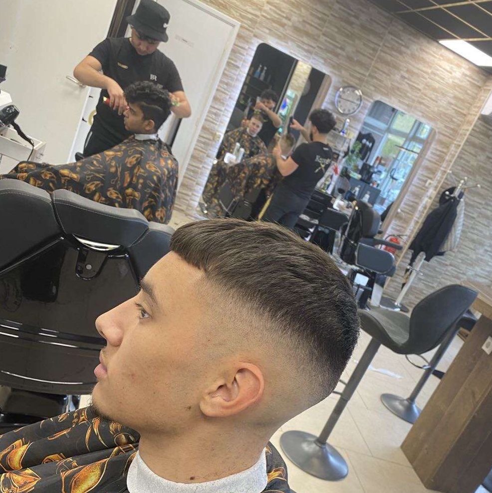 Jonge klant met een skin fade, op de achtergrond kappers aan het werk